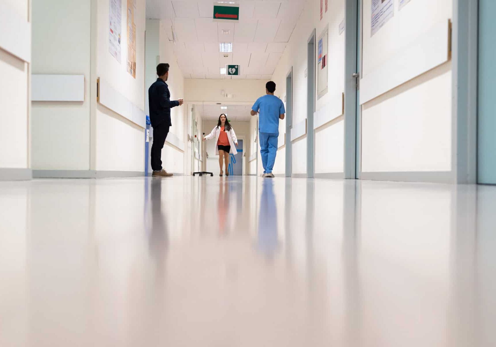 Female medic running in hall of hospital beneath people.